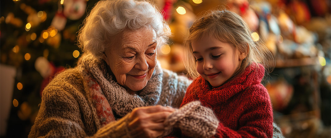 An elderly woman with her granddaughter smiling down at a gift in their hands.